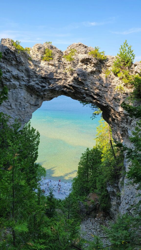 Stunning natural limestone arch known as Arch Rock, perched high above the sparkling blue waters of Lake Huron. A breathtaking geological formation and iconic landmark on Mackinac Island in Michigan.